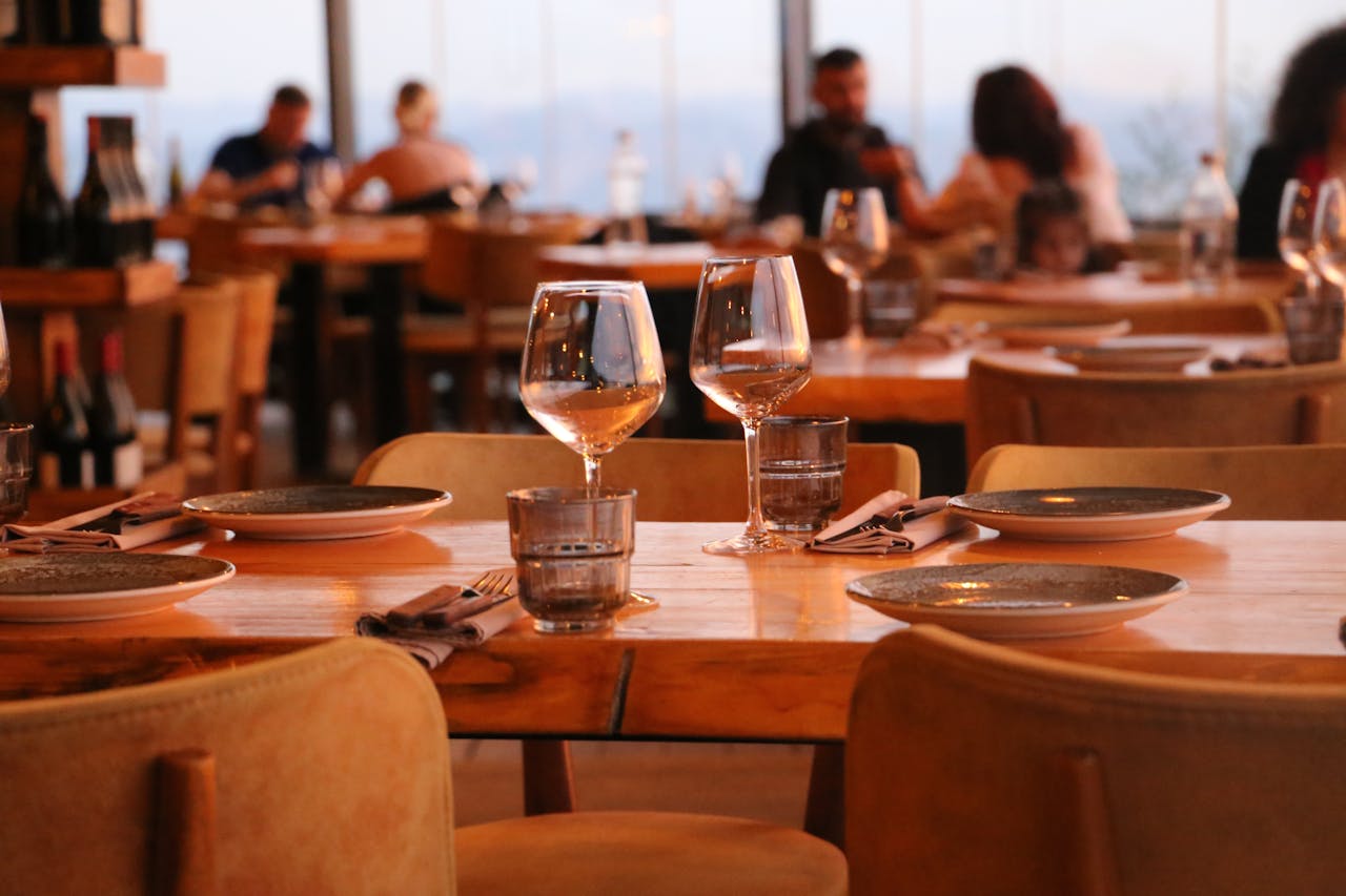 Home A warmly lit restaurant table set with glassware, plates, and napkins ready for a meal.