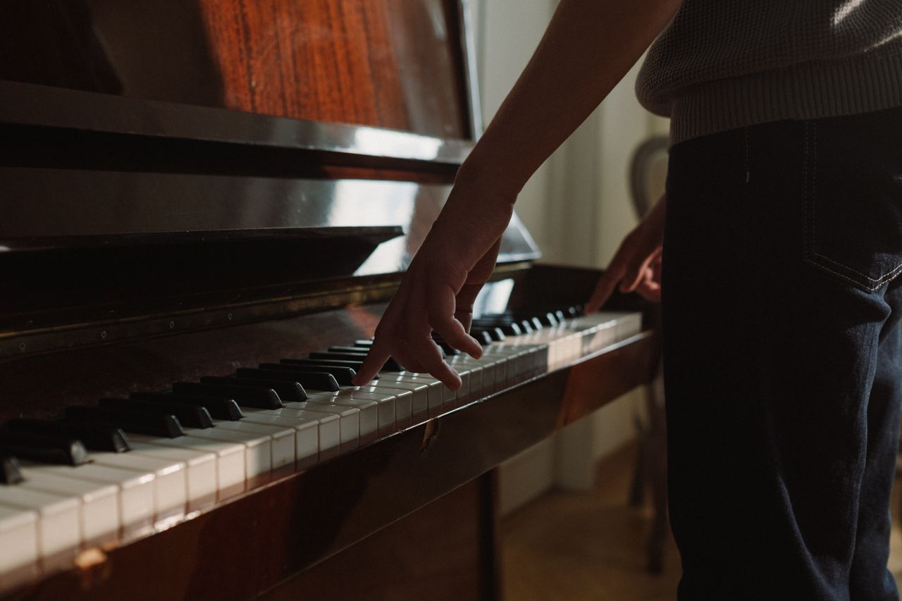 A person playing piano keys on an upright piano indoors, capturing a musical moment.