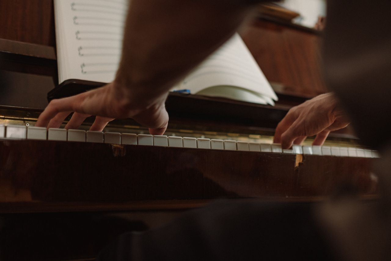 Artistic shot of hands playing piano keys with a music sheet in the background.