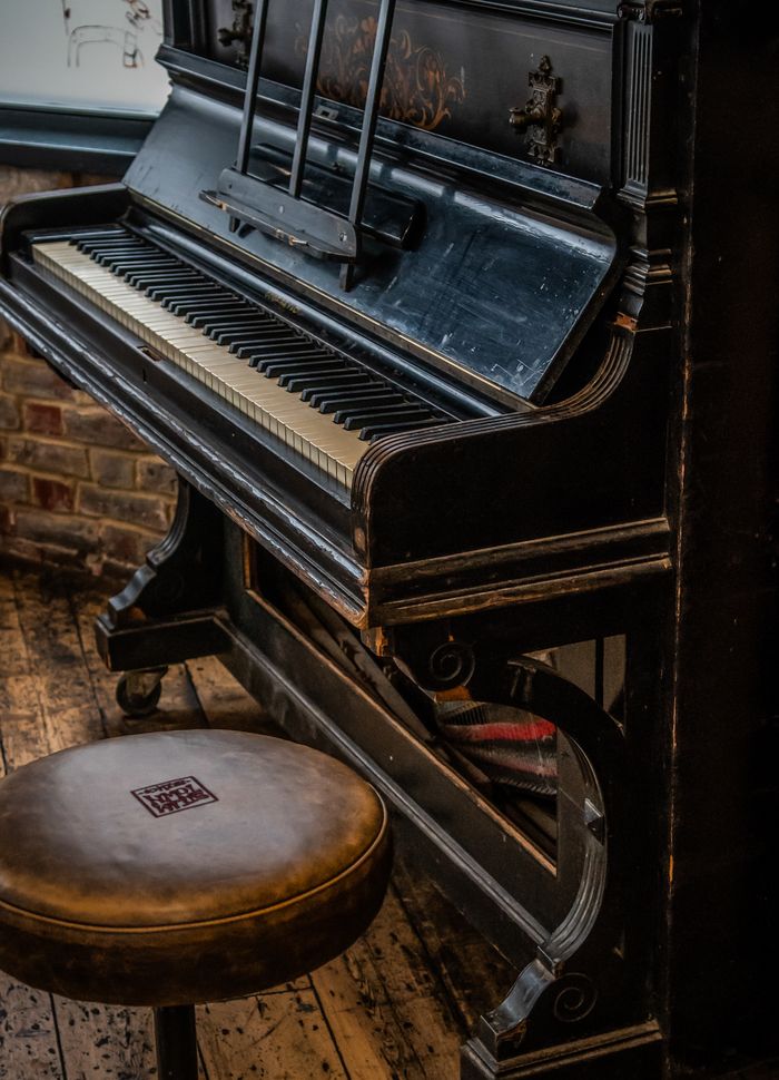 A classic vintage upright piano paired with a leather stool in a cozy, rustic indoor setting.